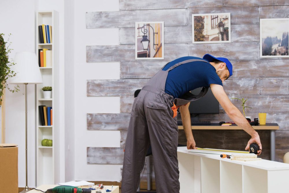 Furniture assembly worker standing reading instruction and using a tape measure. Worker tools.